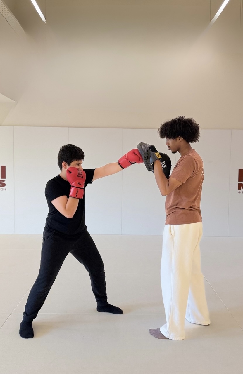 A teenager working boxing pads with a coach in the MOGA training hall